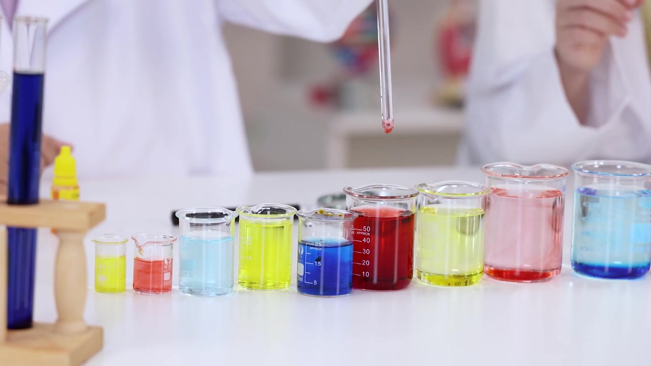 Uno scienziato usa una pipetta di vetro per mescolare liquidi colorati in becher durante esperimenti di chimica