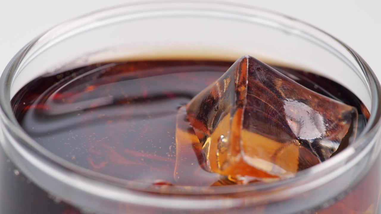Primo piano di cubetti di ghiaccio che cadono in un bicchiere di cola fresca su sfondo bianco