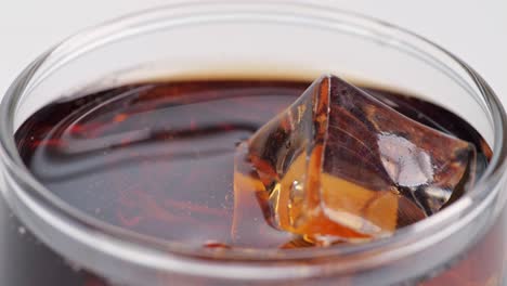 close up of ice cubes falling in a glass of fresh cola on white background