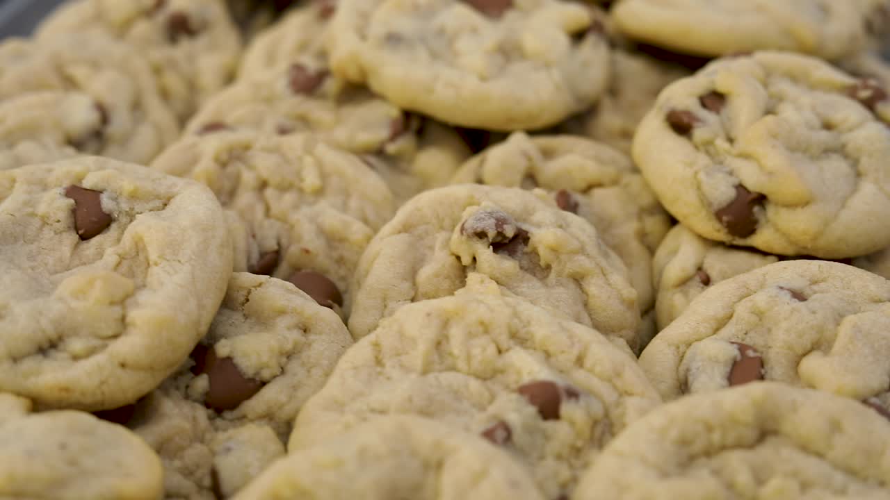 Delicious cooked chocolate chip cookies piled on pan ready to be eaten, close up above pan left