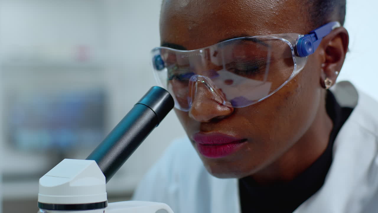 Primo piano di una dottoressa africana che analizza un virus al microscopio