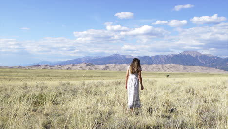 Die-Großen-Sanddünen-Des-Colorado-Nationalparks,-Spätsommer,-Schöne-Frau,-Model,-Schauspielerin,-Sonne-Geküsst,-Friedlich,-Glücklich,-Entspannt,-Gehen,-Hohes-Goldenes-Gras,-Süßes-Kleid-Mit-14er-Berggipfeln,-Filmisch