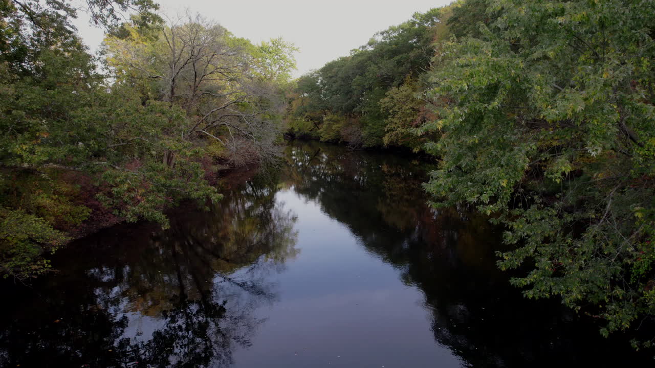 Aerial drone video of the peaceful Pawtuxet River in Cranston, Rhode Island lined with color changing fall foliage and bookended by a railroad bridge and a road bridge