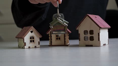 llavero con las llaves de la casa en la mano. casas de juguete en la mesa. compra de bienes raíces. transacción inmobiliaria