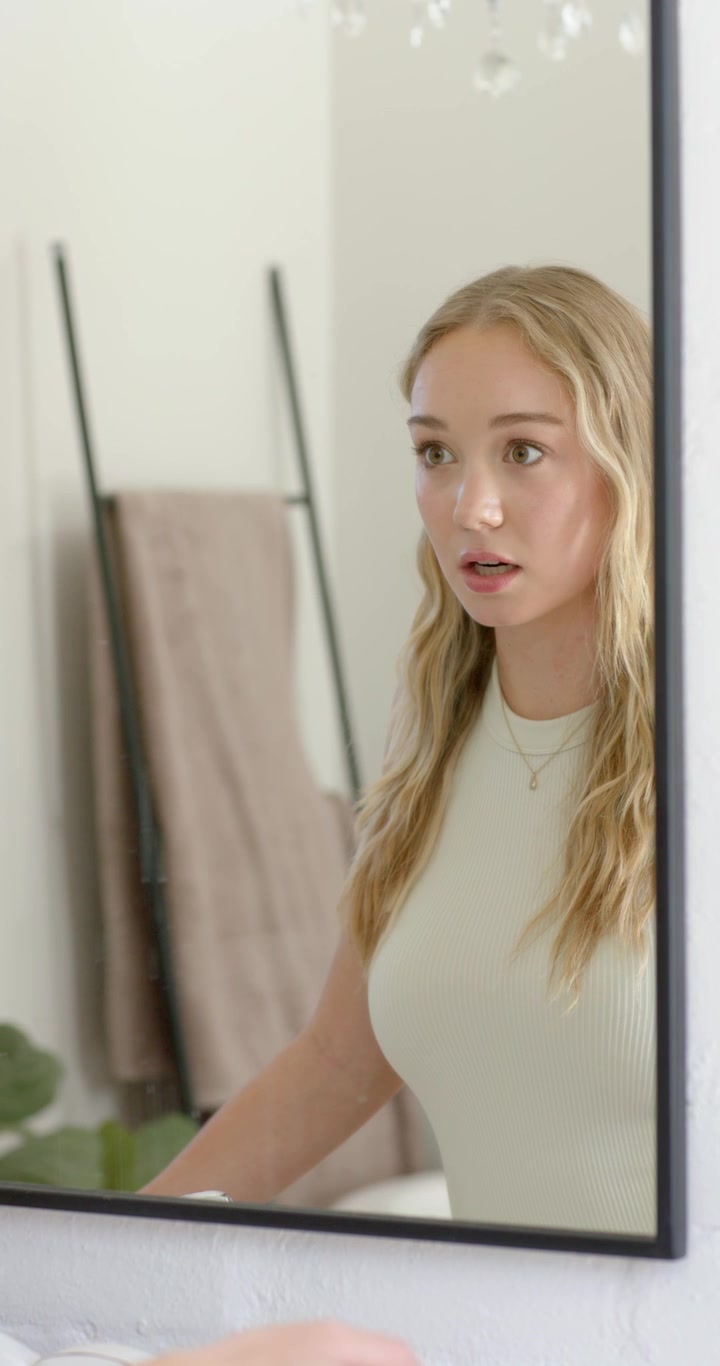 Video verticale: Donna che si guarda allo specchio, lisciandosi i capelli mossi allo specchio del bagno e controllando le collane.