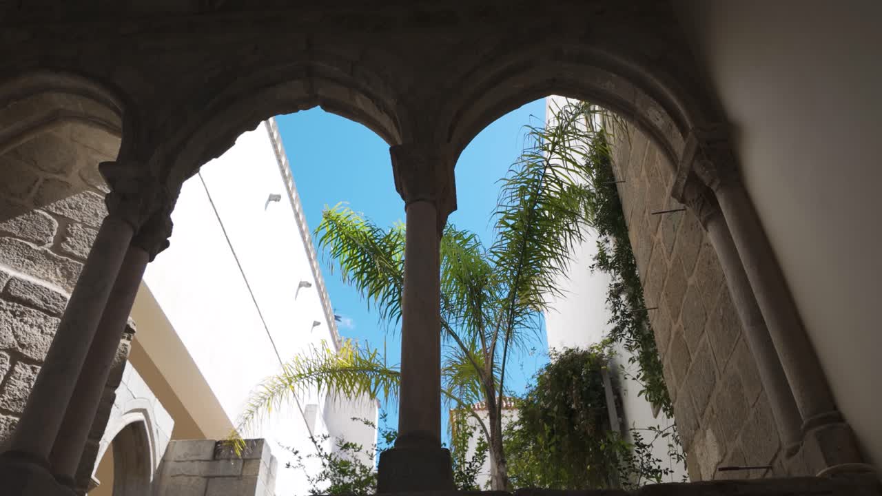 View of a stone arch with palm trees and clear sky at the Chapel of Bones in Évora