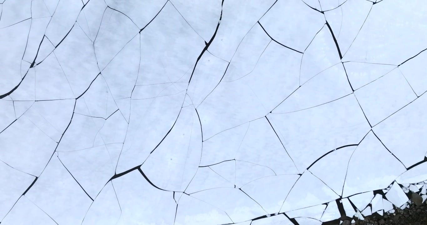 Stortvatnet lake on Austvagoya in Vagan Nordland Norway shows thermal contraction cracks across frozen surface forming polygon network with subtle reflection, ascending top down drone barrel roll