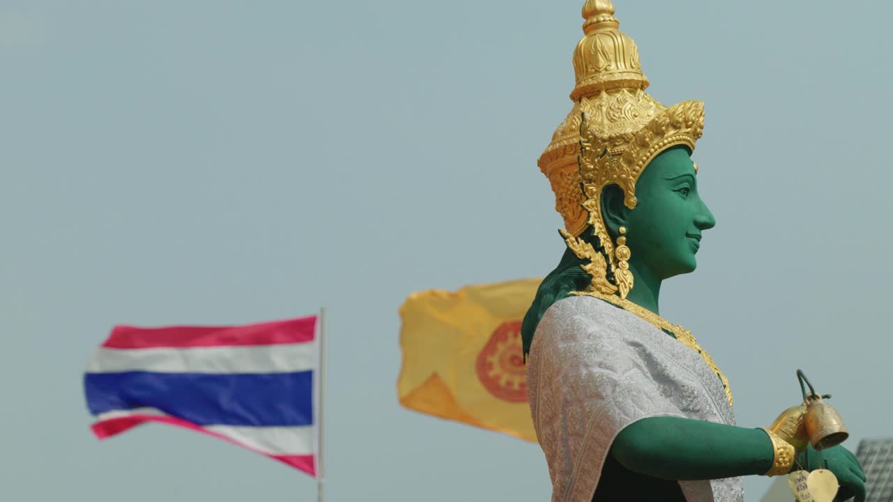 imágenes cinematográficas en cámara lenta de 4k de una estatua dorada y verde de una figura religiosa budista en la parte superior del templo del monte dorado en bangkok, tailandia, con la bandera de tailandia moviéndose en el fondo