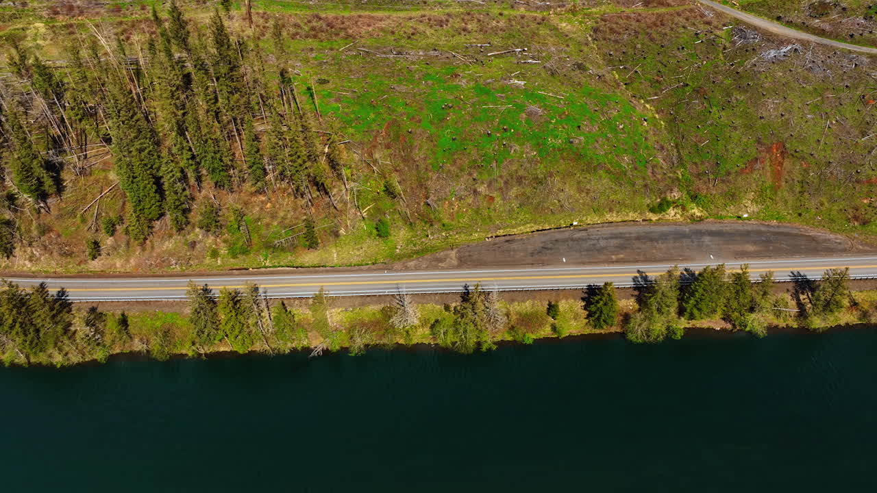 Quickly moving car on the highway at the waterfront of river. Mountainous landscape with dry cut wood scattered around. Top perspective.