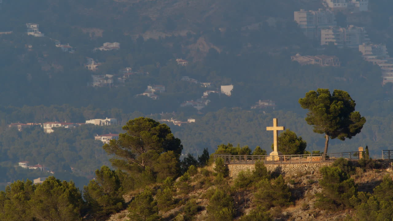 escena de una ciudad de montaña con la cruz cristiana en la colina en la nucia, españa