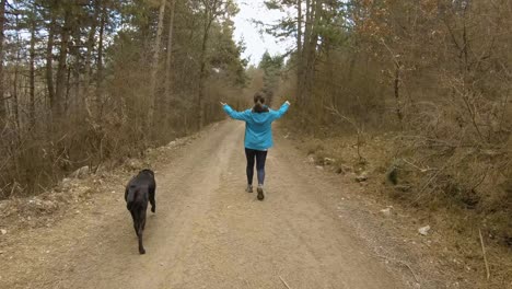 girl walking on mountain trail in forest with black dog, during autumn