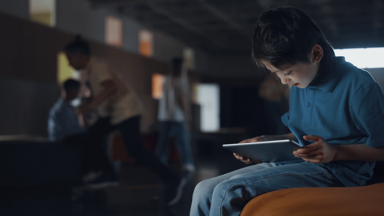Teen boy sitting holding tablet in school hall. Pupil playing game online.