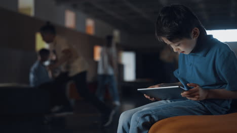 Teen-boy-sitting-holding-tablet-in-school-hall.-Pupil-playing-game-online.