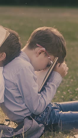 sleeping pupil fixes pen in mouth to hold book leaning on schoolmate dreaming with book on green garden lawn slow motion