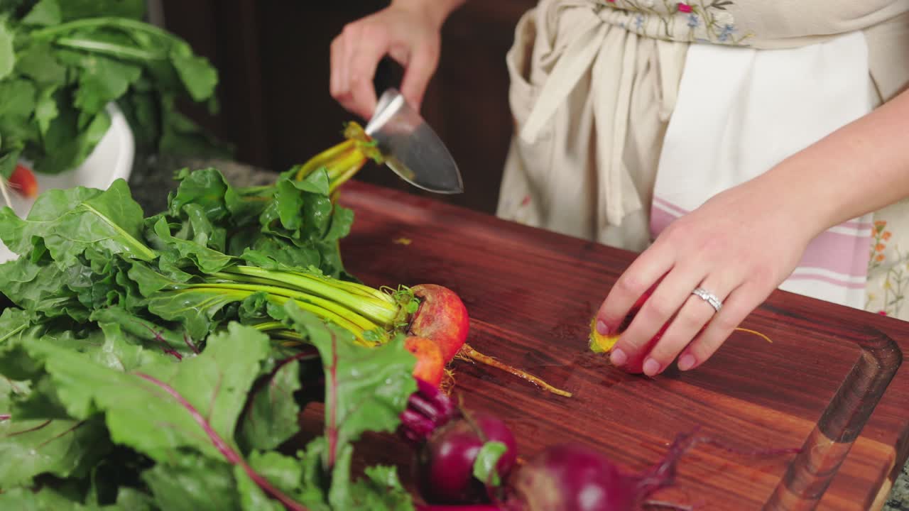 una persona cortando remolachas frescas y verduras en una tabla de cortar de madera en el interior
