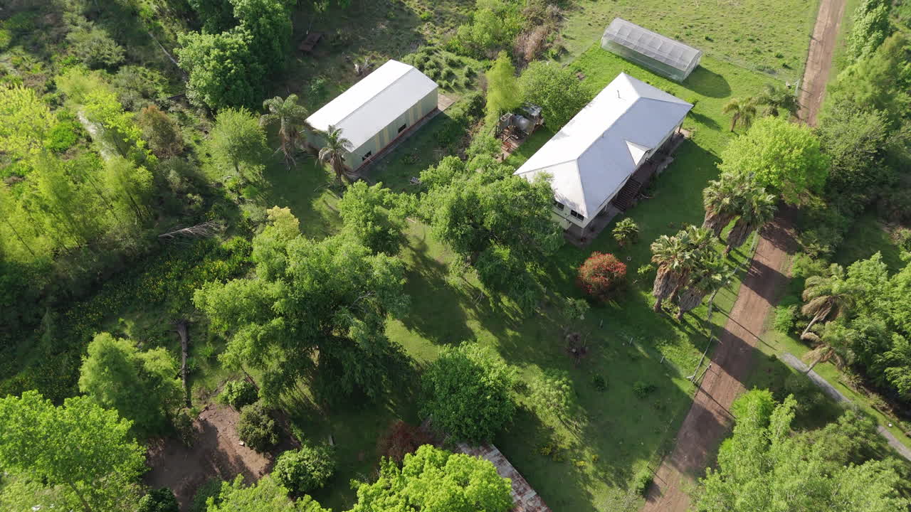 Aerial high angle overview of rural school buildings surrounded by dense greenery in forest area under early morning light