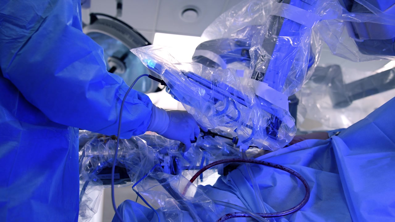 Cooperation of male surgeon and robotic surgical system. Doctor holds the tool while manipulative arm moves in patient's body.