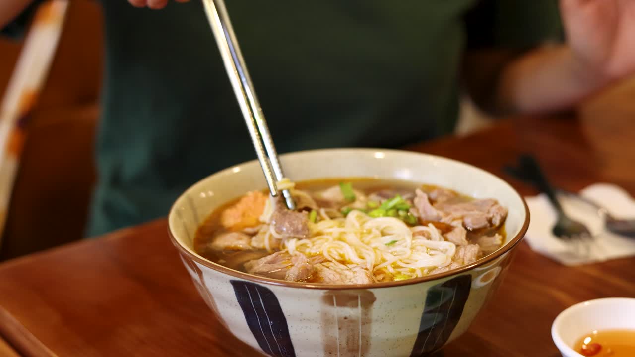 Cận cảnh đôi tay dùng đũa gắp bún từ bát phở bò