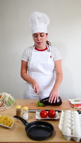 female cook cutting eggplant on wooden board in kitchen.