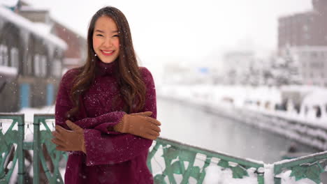 static shot of a asian woman, standing cold and smiling, in the snowfall, in otaru, hokkaido, japan