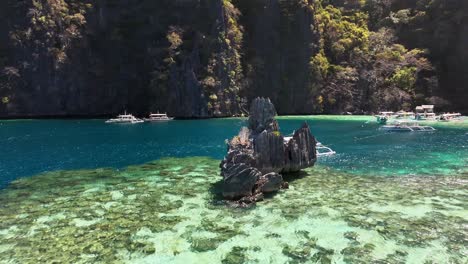 a towering limestone rock emerges from crystal-clear turquoise waters, surrounded by coral reefs, boats, and dramatic cliffs in the serene tropical setting of twin lagoon, coron, philippines
