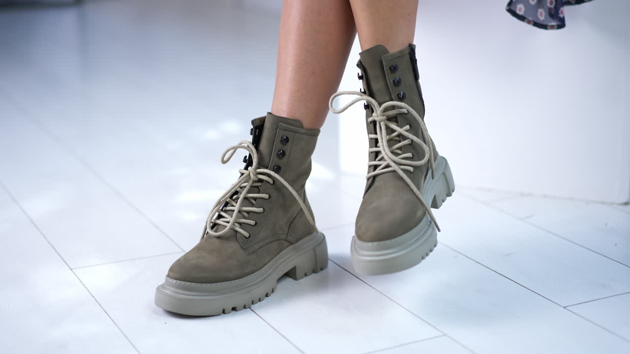 Model ties the laces on the modern boots. Sitting female demonstrating grey fashionable footwear. Close up.