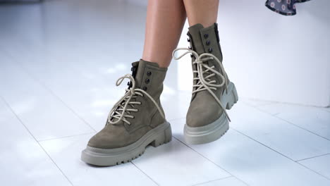 model ties the laces on the modern boots. sitting female demonstrating grey fashionable footwear. close up.