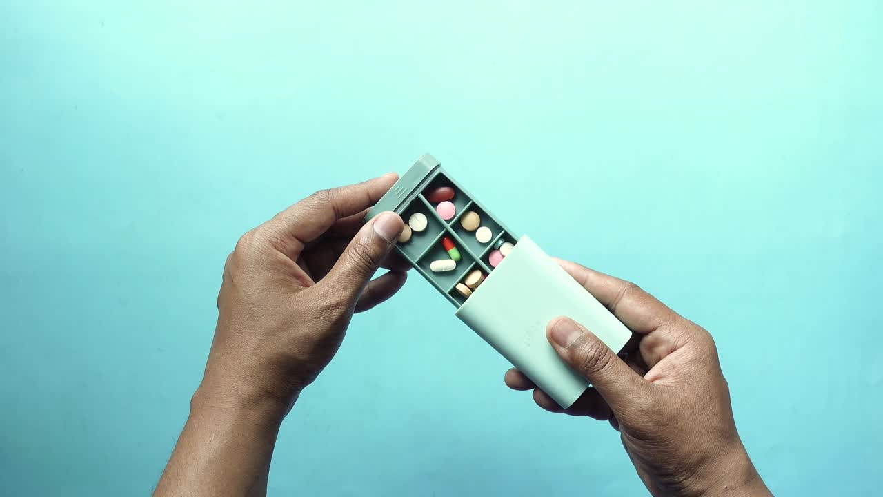 Hands holding a pill organizer with various pills inside