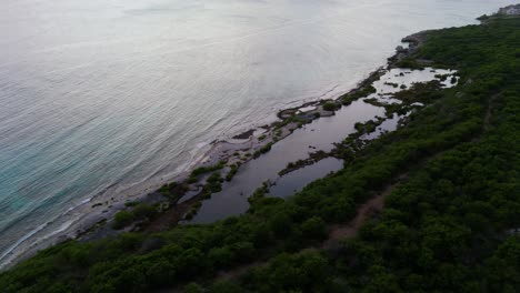 Natural-tide-pools-form-at-low-tide-as-sunset-light-glistens-on-calm-ocean-water,-Piscadera-Curacao