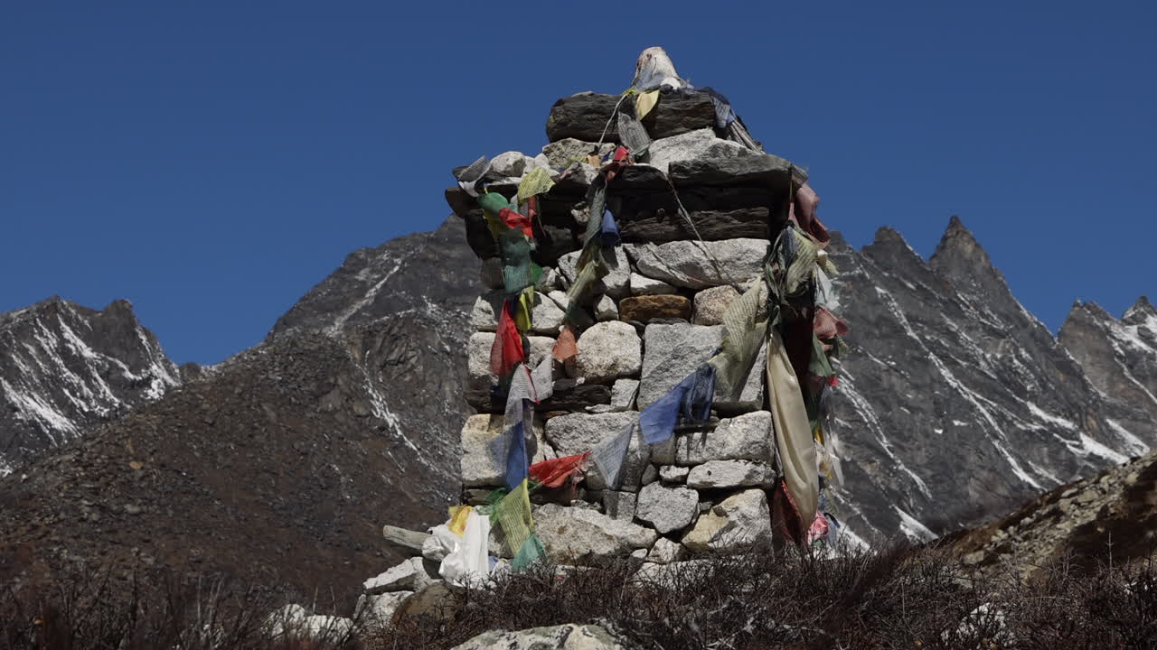 Rock stack with flags on a trail in Nepal with mountains in the background.