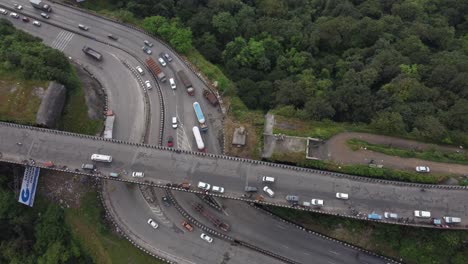 Filmische,-Nach-Oben-Geneigte-Luftaufnahme,-Die-Eine-Schöne-Autobahnkreuzung-Mit-Autos-Und-Schweren-Transportfahrzeugen-Zeigt,-Die-Sich-Kreuzen,-Und-Eine-Von-Bergen-Umgebene-Stadt