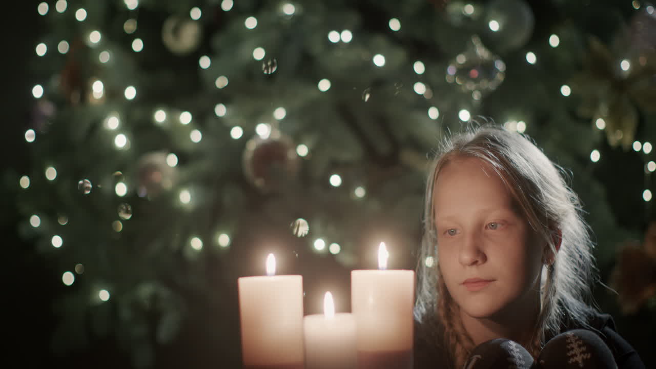 el niño mira la vela encendida en sus manos. con el telón de fondo de las luces borrosas del árbol de navidad. pide un deseo