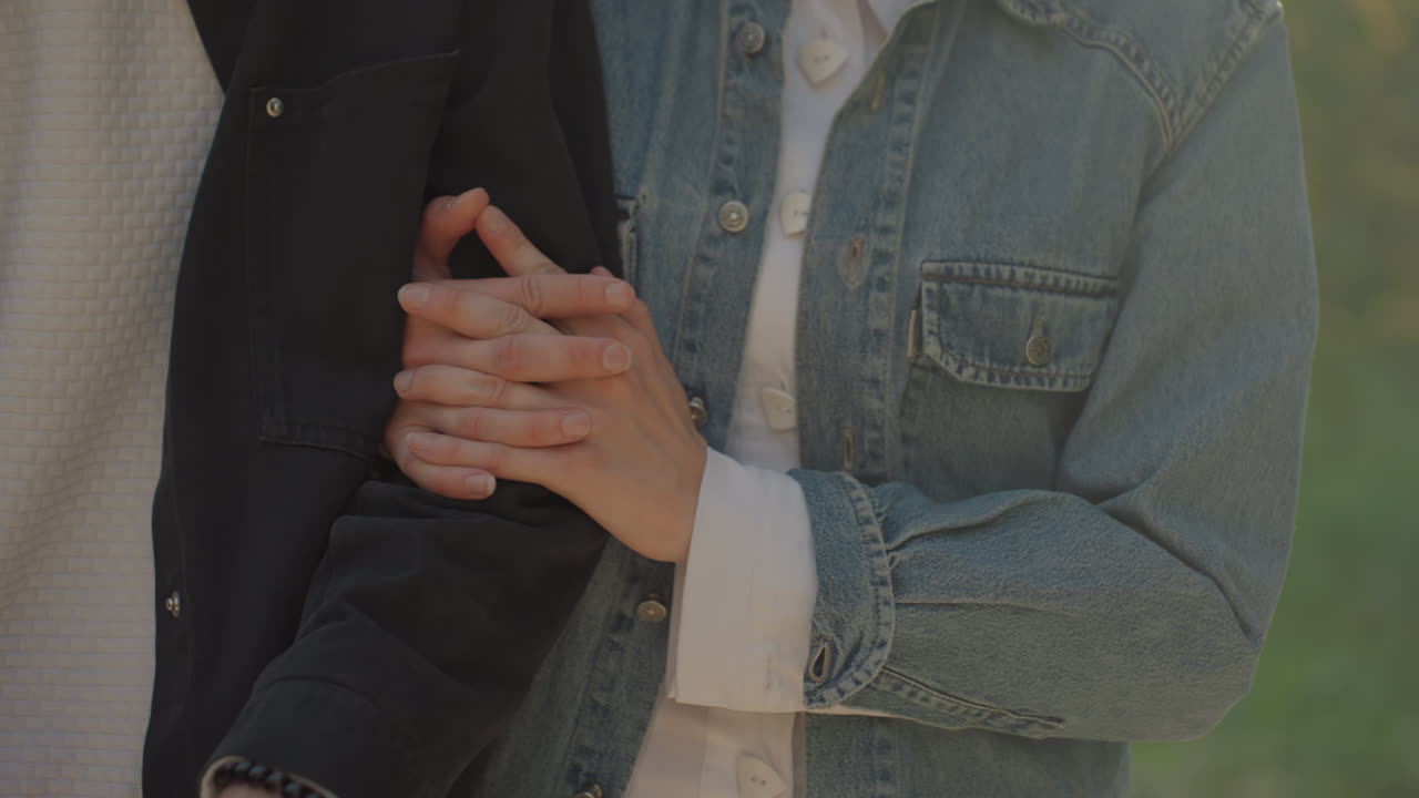 Coppia che si tiene per mano godendosi una giornata di sole. Due persone che condividono momenti teneri durante una passeggiata all'aperto di giorno. Uomo e donna si abbracciano gioiosamente mentre fanno una tranquilla passeggiata all'aperto in un parco di giorno