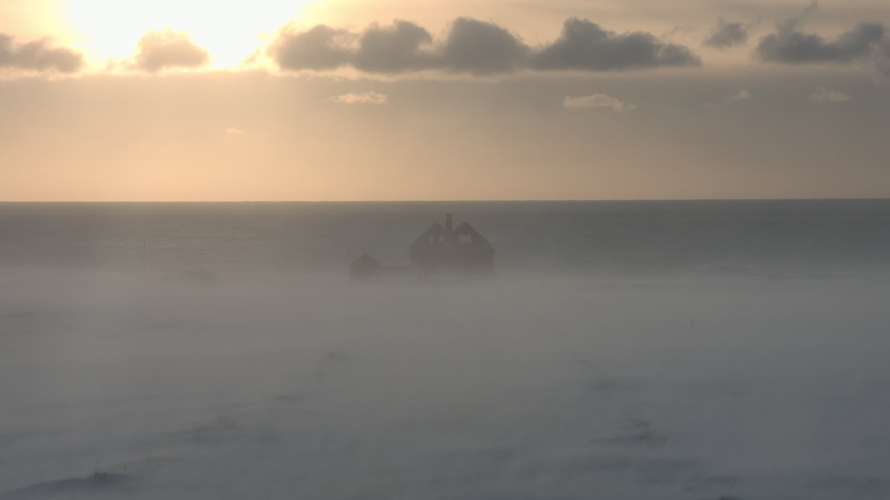 해가 지는 동안 안개가 가득한 해안선에 있는 폐허가 된 집