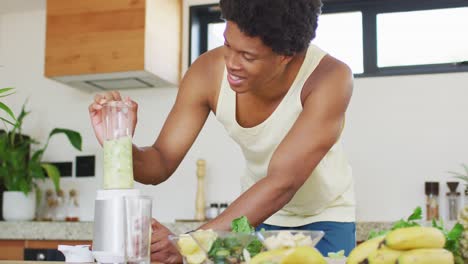 fit african american man cooking, preparing healthy green smoothie