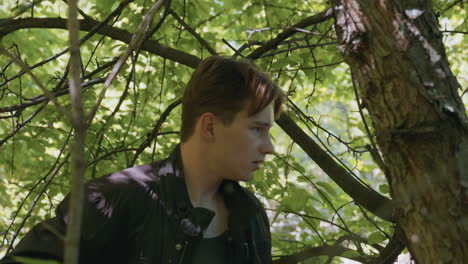 adventurer under leafy canopy slips off jacket with cautious gaze surveying surroundings while dappled sunlight filters through branches illuminating forest backdrop with tense mood of exploration
