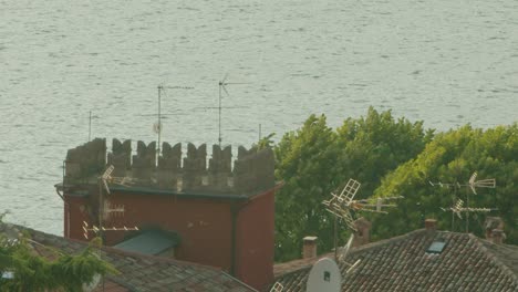 slow motion shot, a bird flying through the top of the roof top in malcesine in italy, lago di garda in the background