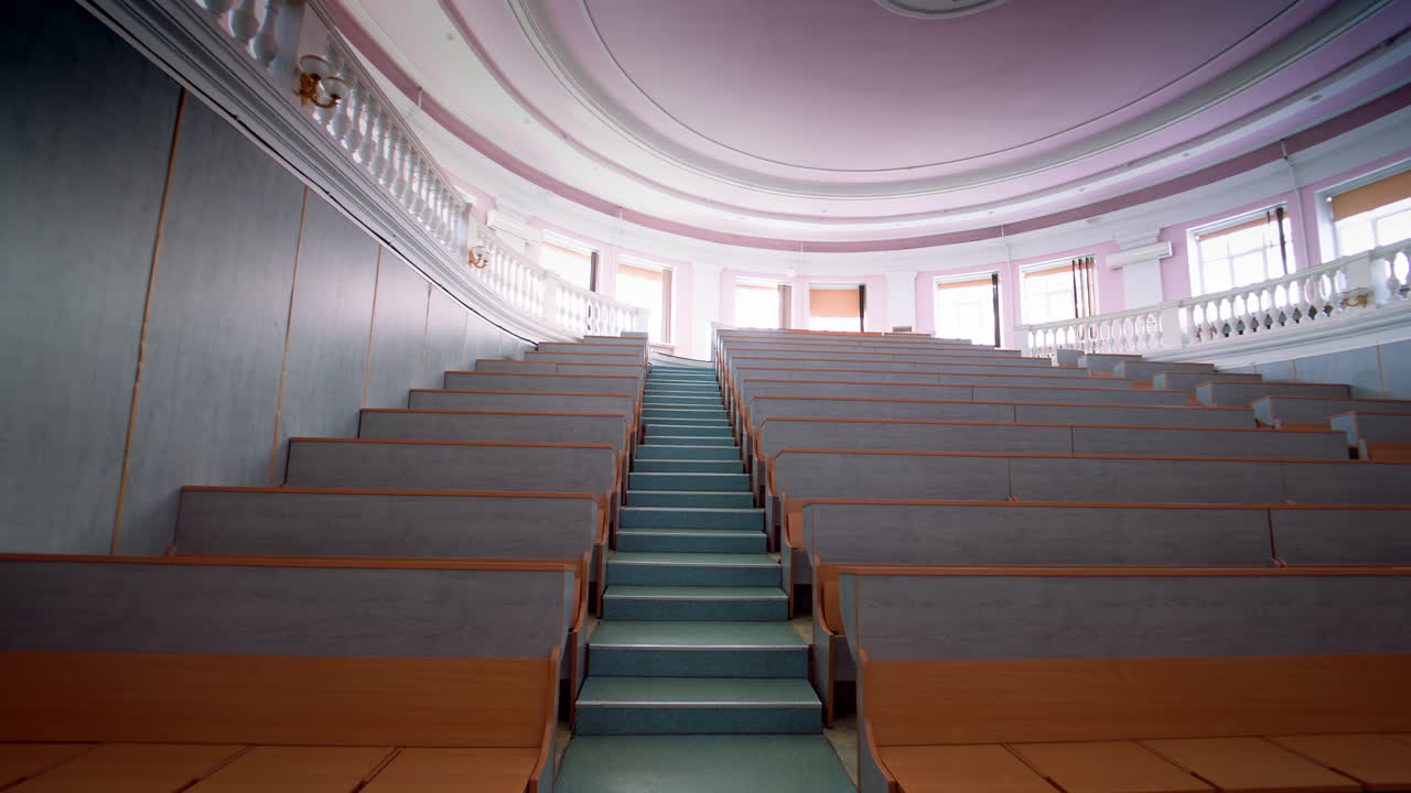Modern auditorium with stairs. Many rows of wooden desks rising up in the conference hall. Spacious classroom for lectures in the university.