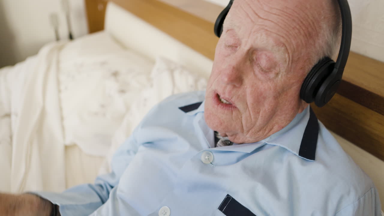 Elderly man listening to headphones in bed