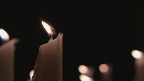 an extreme close up of white candles lit with a black background in slow motion