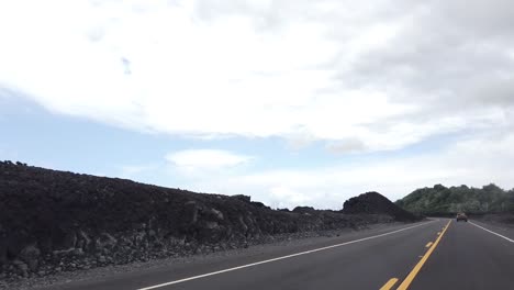 drive through a lava field on a paved road one year after an eruption with blue skies and clouds.