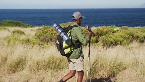 african american man hiking with hiking poles in countryside by the coast