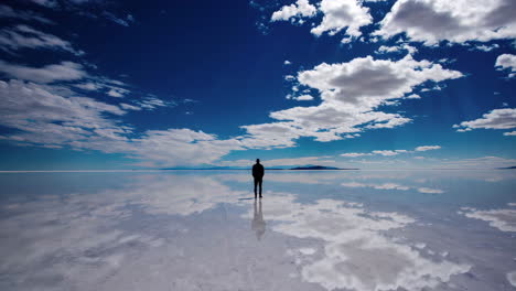 a solitary figure stands on a vast, reflective salt flat under a wide blue sky