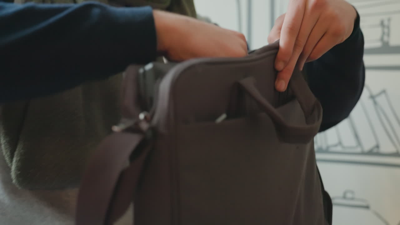 Mani che preparano il laptop su un tavolo con candela e luci, primo piano delle dita che chiudono la borsa imbottita, maglione morbido e jeans visibili, bagliore ambientale caldo, tranquilla routine mattutina prima del tragitto.