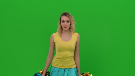 a cheerleader dances a jubilant dance, crouches gracefully, does vertical splits, waves her hair. a blonde in a yellow-blue uniform is training in the studio on a green screen. close up. slow motion