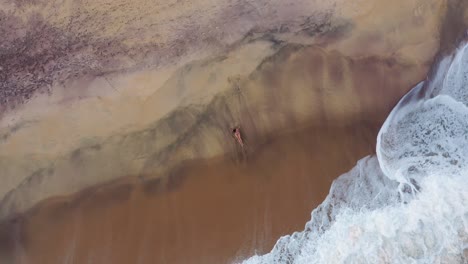 Top-aerial-view-of-sand-beach-at-sunset-with-beautiful-young-slim-woman-sunbathing-lying-on-a-beach