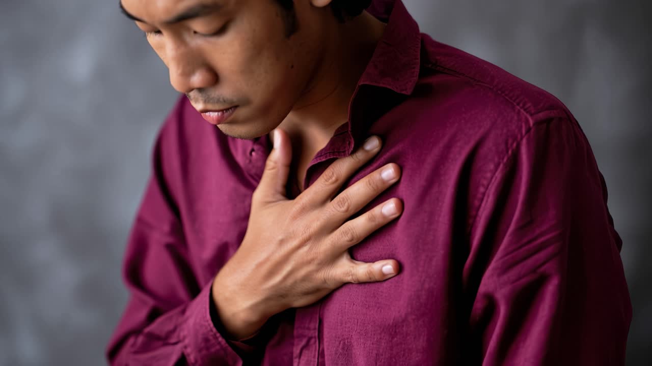 Man places hand over chest, showing distress. He leans forward, eyes closed, breathing heavily. His expression suggests pain or anxiety. Suitable for medical, wellness, or health-related content