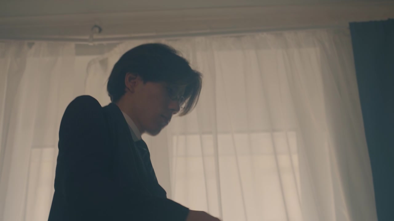ドレープのある暖かな逆光の部屋で、近くにブリーフケースを置いた若いアジア人男性がジャケットを羽織っている。素早いネクタイの調整、集中した表情。面接や会議の準備をしており、綿密な身だしなみ。映画のような色調。