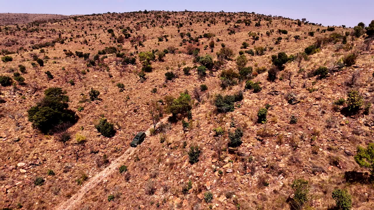 4x4 Truck drives cautiously down track in rocky and rugged mountain. Drone view