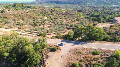 Sobre-La-Carretera-Y-El-Bosque-Verde-En-Rodas-Con-La-Playa-Al-Fondo-En-Grecia-Durante-El-Verano-Filmado-Con-El-Dron-En-4k